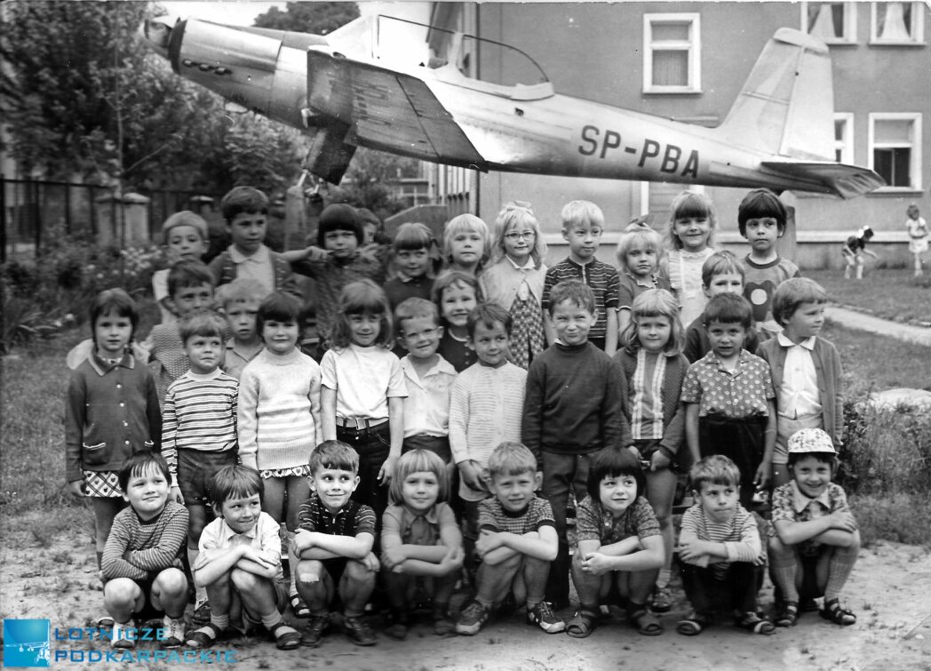 dzieci stoja na tle samolotu przed budynkiem